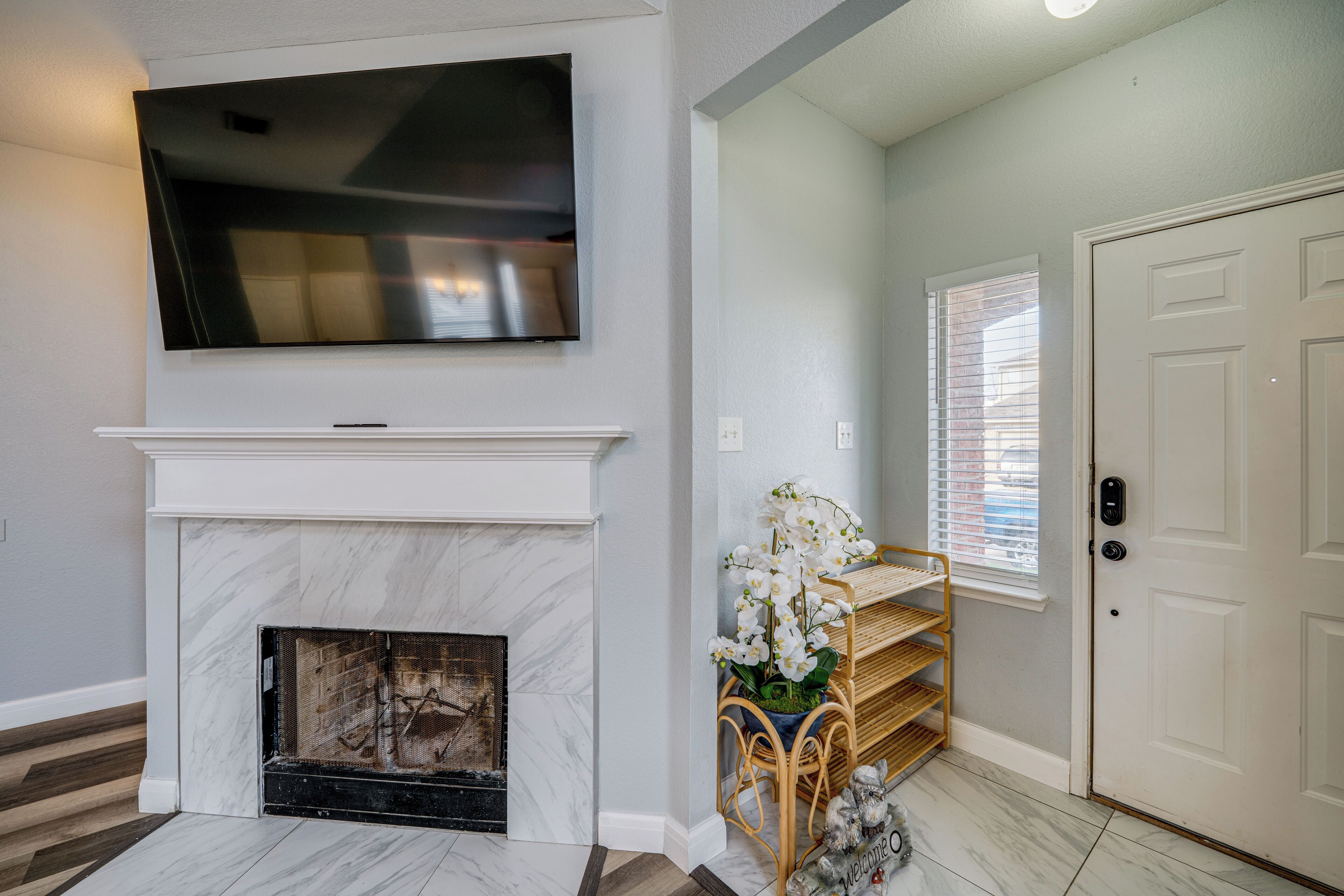 A living room with a fireplace, a mounted TV, a door, and a window with blinds.