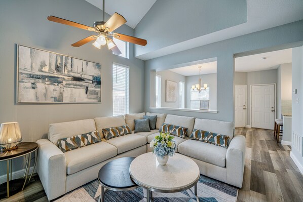 A living room with a sectional sofa, a round coffee table, a ceiling fan, and a large abstract painting. - Pet Friendly! Renovated Arlington Home Near At&t (Arlington)