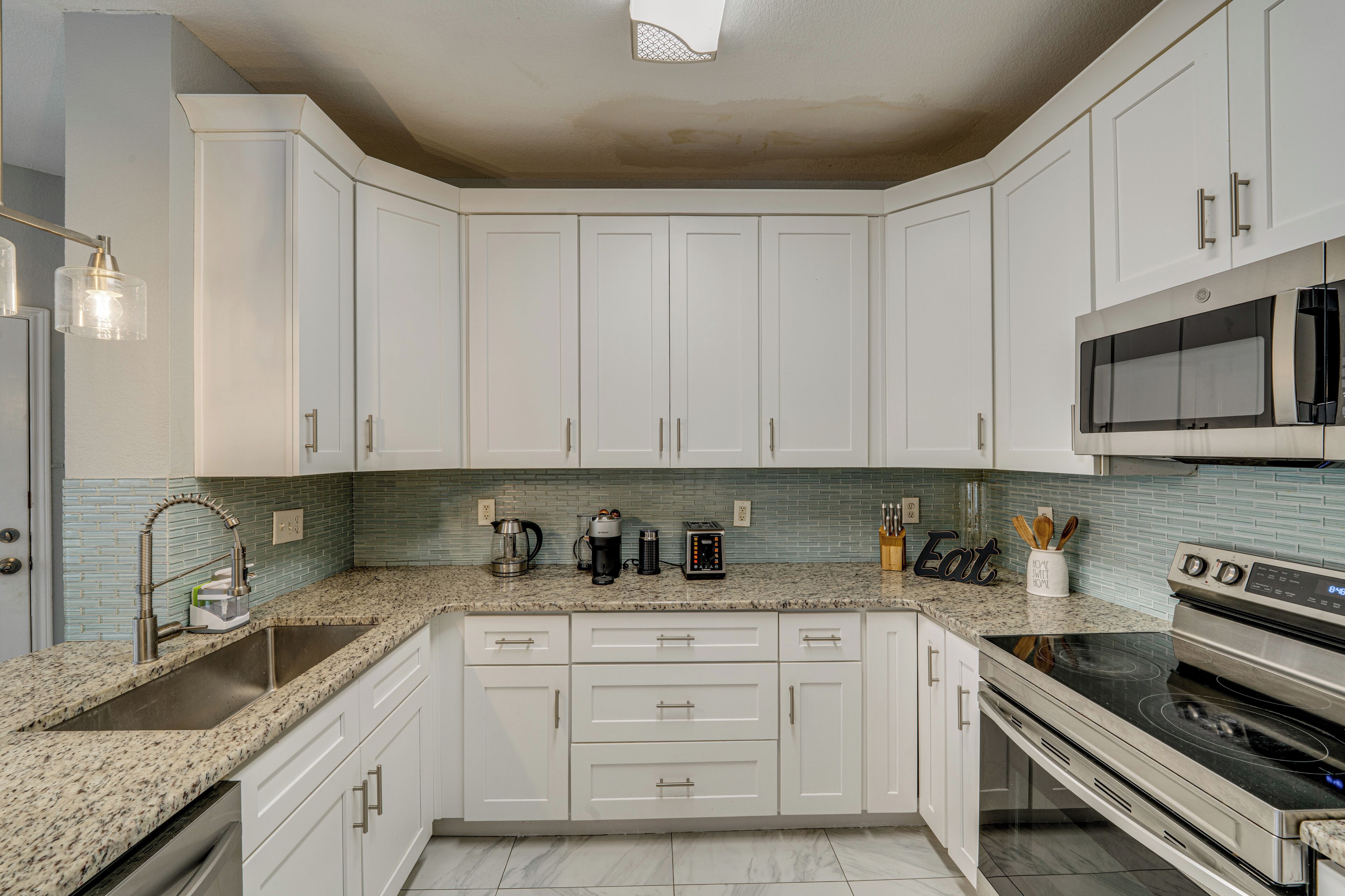 A kitchen with white cabinets, a granite countertop, a stainless steel sink, a microwave, and an oven.