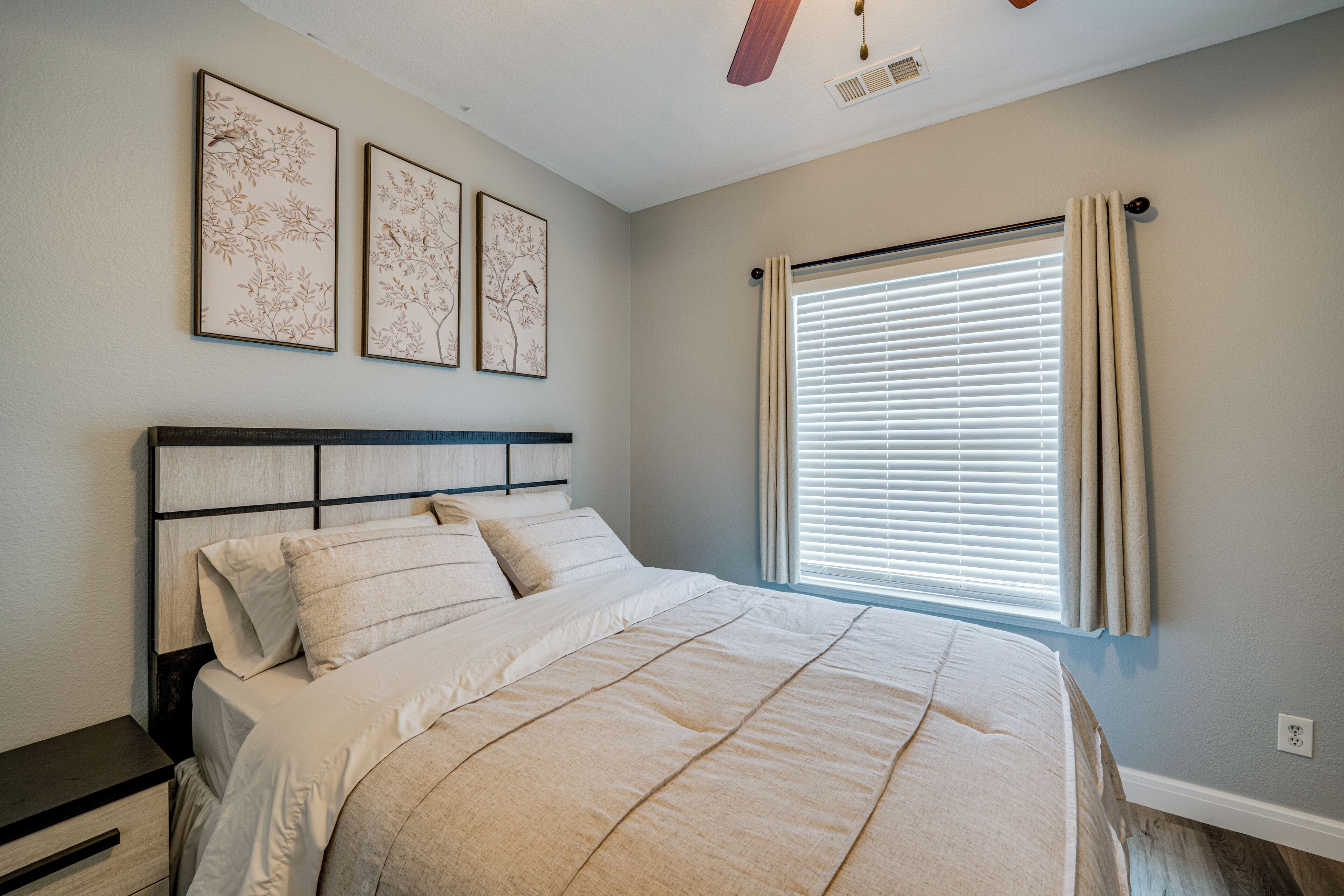A bedroom with a bed, a nightstand, a ceiling fan, and a window with curtains.