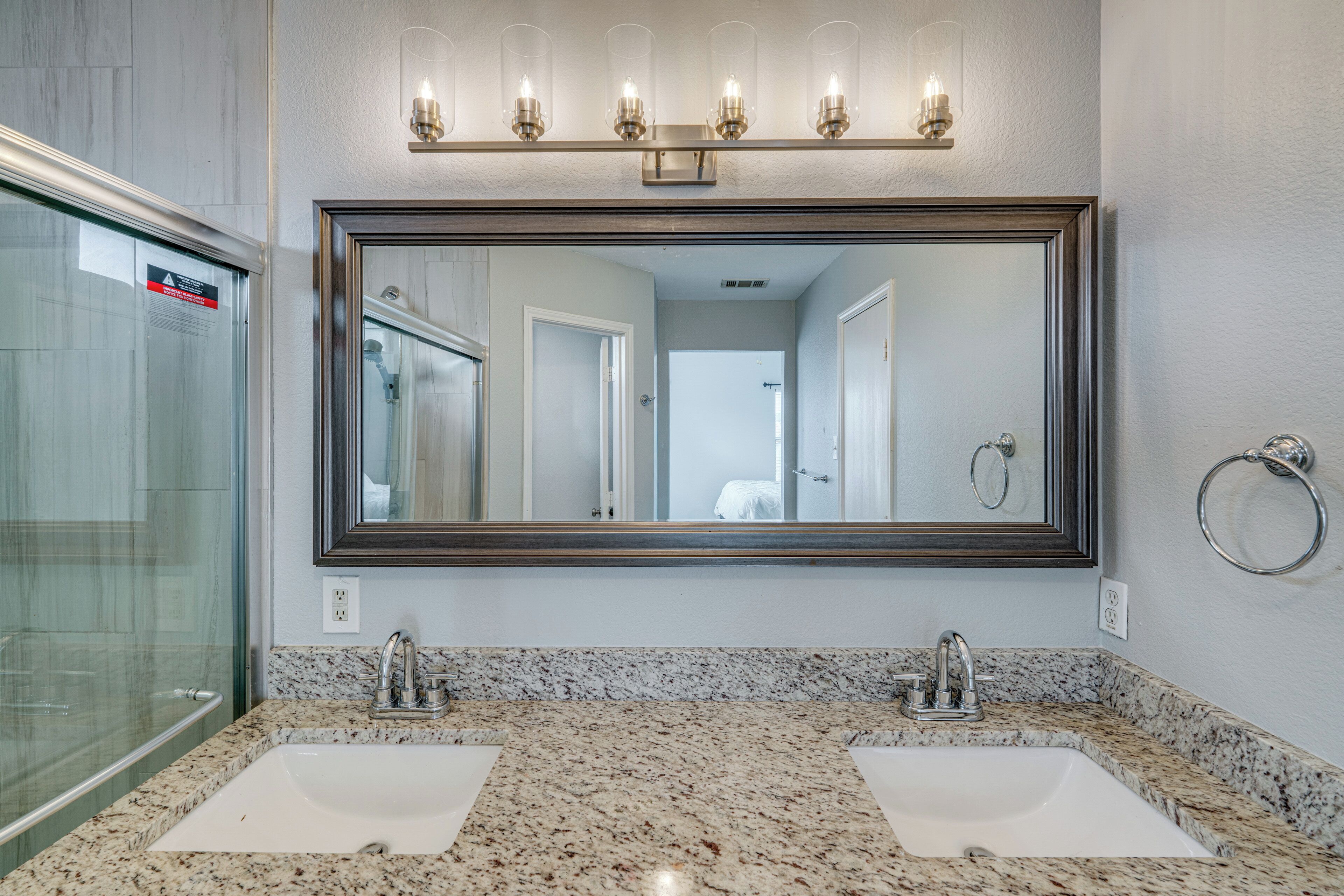 A bathroom with a large mirror, two sinks, a shower, and a glass-enclosed shower area.