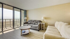 A room with a balcony, a grey sofa, a beige sofa, a small table, and a nightstand with lamps. - Oceanfront Myrtle Beach Getaway w/ Balcony (Myrtle Beach)