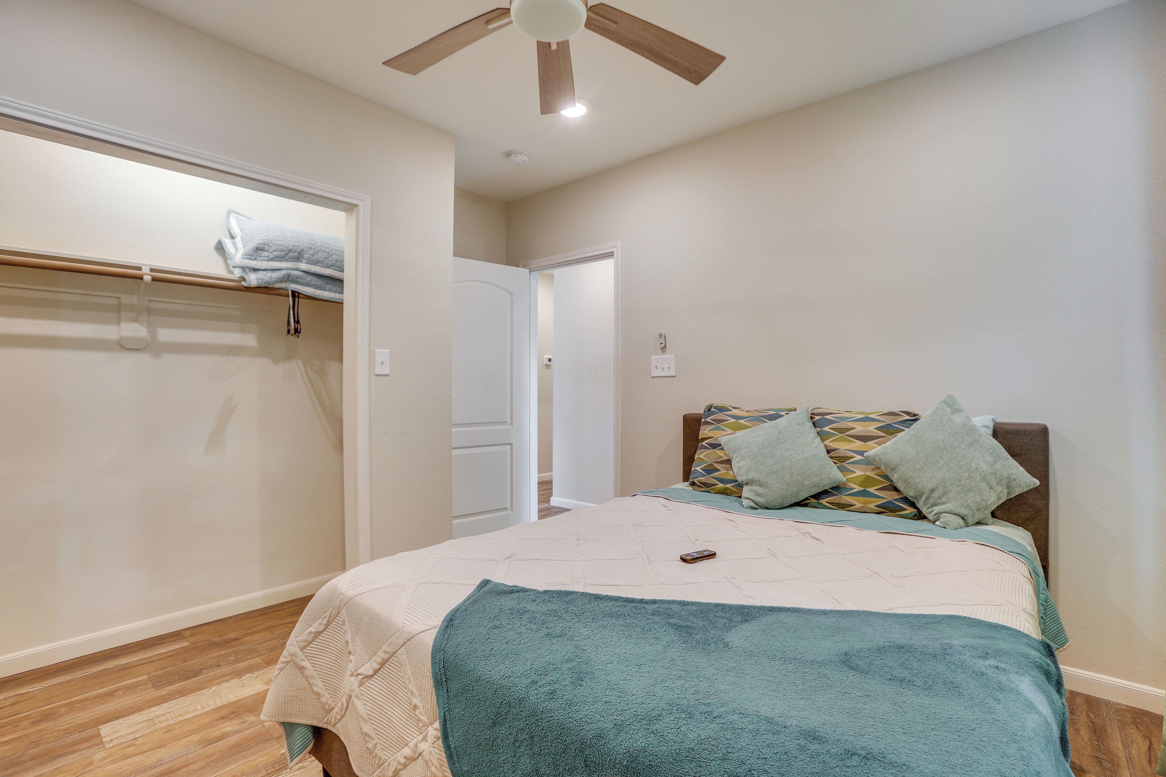 A bedroom with a bed, a ceiling fan, a door, and a towel rack.