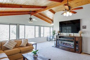 A living room with a sofa, coffee table, fireplace, television, and large windows.