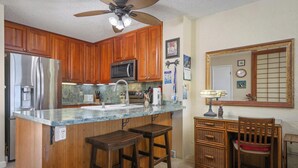 A kitchen with wooden cabinets, a stainless steel refrigerator, a microwave, a sink, and a bar stool. - Top Floor Oceanfront Condominium in Kailua-kona (Kailua-Kona)