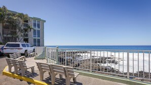 A beachside view with a white building, benches, and a white car parked near the shore. - Top Floor Oceanfront Condominium in Kailua-kona (Kailua-Kona)