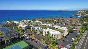 A coastal residential area with multiple-story buildings, a parking lot, and a view of the ocean. - Top Floor Oceanfront Condominium in Kailua-kona (Kailua-Kona)