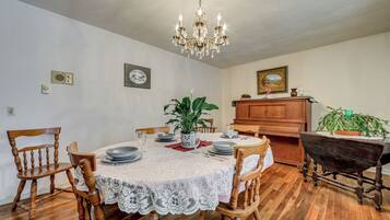 A dining room with a round table, chairs, a chandelier, a piano, and a potted plant.
