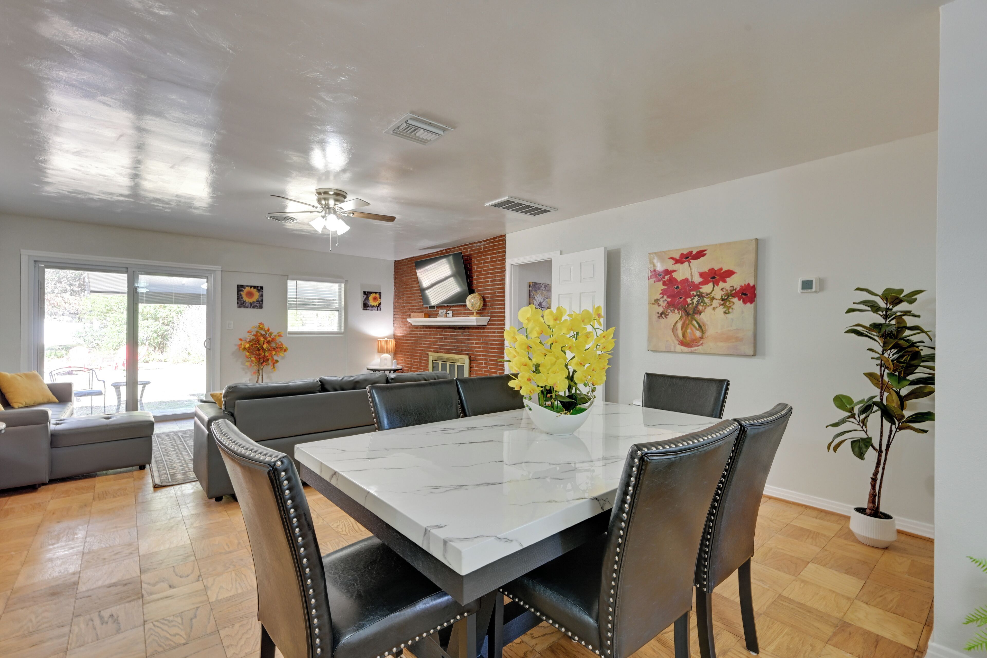 Un coin repas avec une table en marbre, des chaises à revêtement noir, un ventilateur de plafond et une grande fenêtre.
