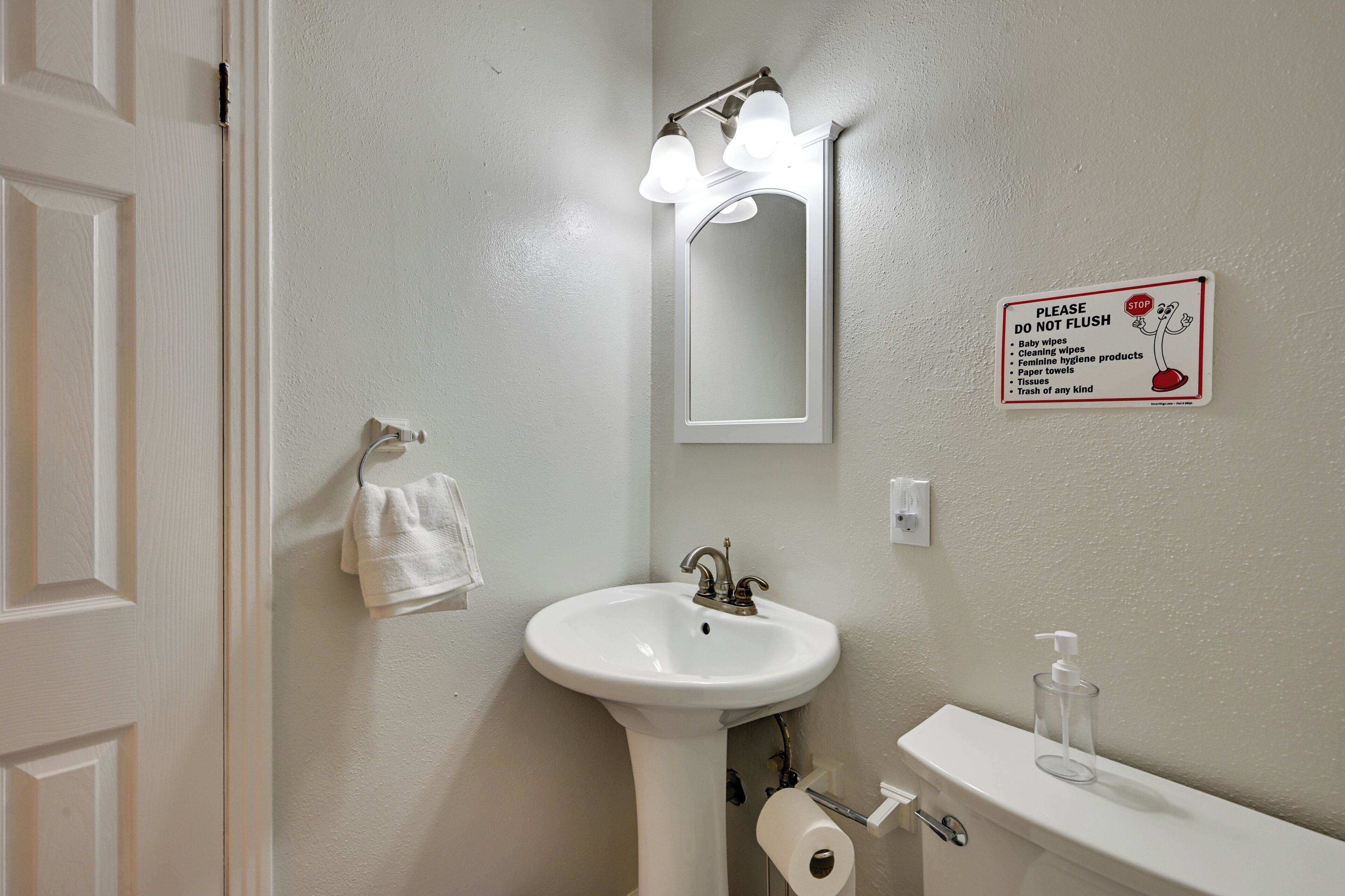 Une salle de bain équipée d’un lavabo, d’un miroir, d’un porte-serviettes et d’une pancarte indiquant : « Veuillez ne pas jeter de déchets dans les toilettes ».