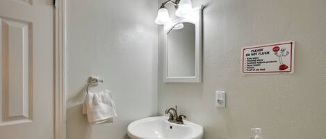 Une salle de bain équipée d’un lavabo, d’un miroir, d’un porte-serviettes et d’une pancarte indiquant : « Veuillez ne pas jeter de déchets dans les toilettes ».