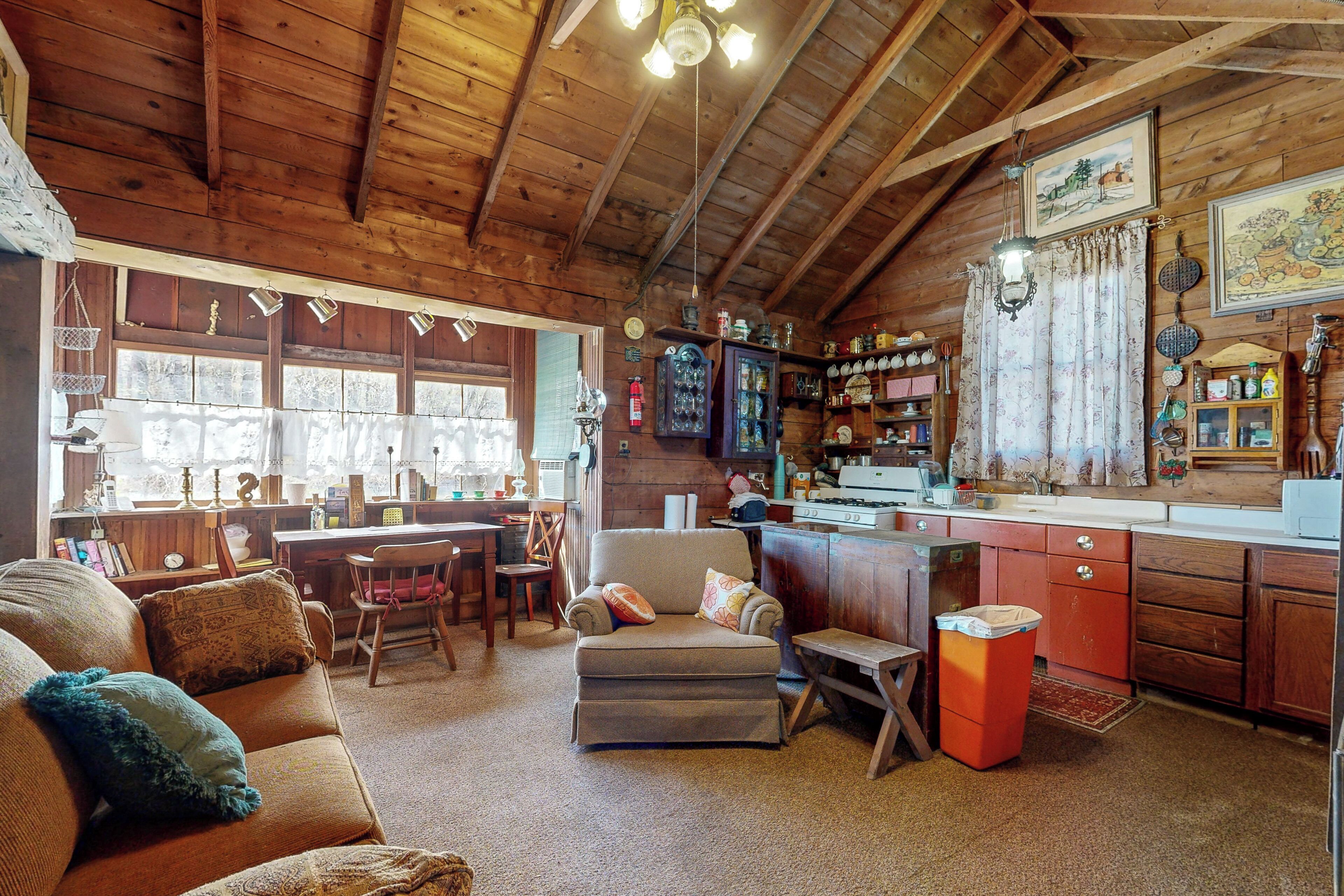 Un interior de cabaña acogedor con techo de madera, comedor, cocina y sala de estar con sofá y reposapiés.