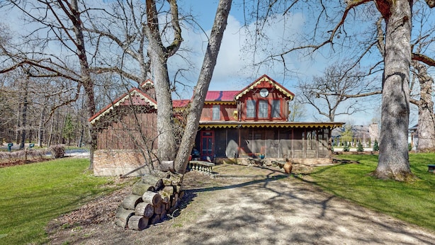 Un bâtiment rustique en bois, avec un toit rouge, entouré d’arbres et bordé d’un chemin de gravier.