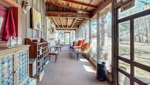 Un espace extérieur aménagé, abrité, avec des bancs et des tables en bois, une grande fenêtre donnant sur les arbres et un panneau avec un logo.