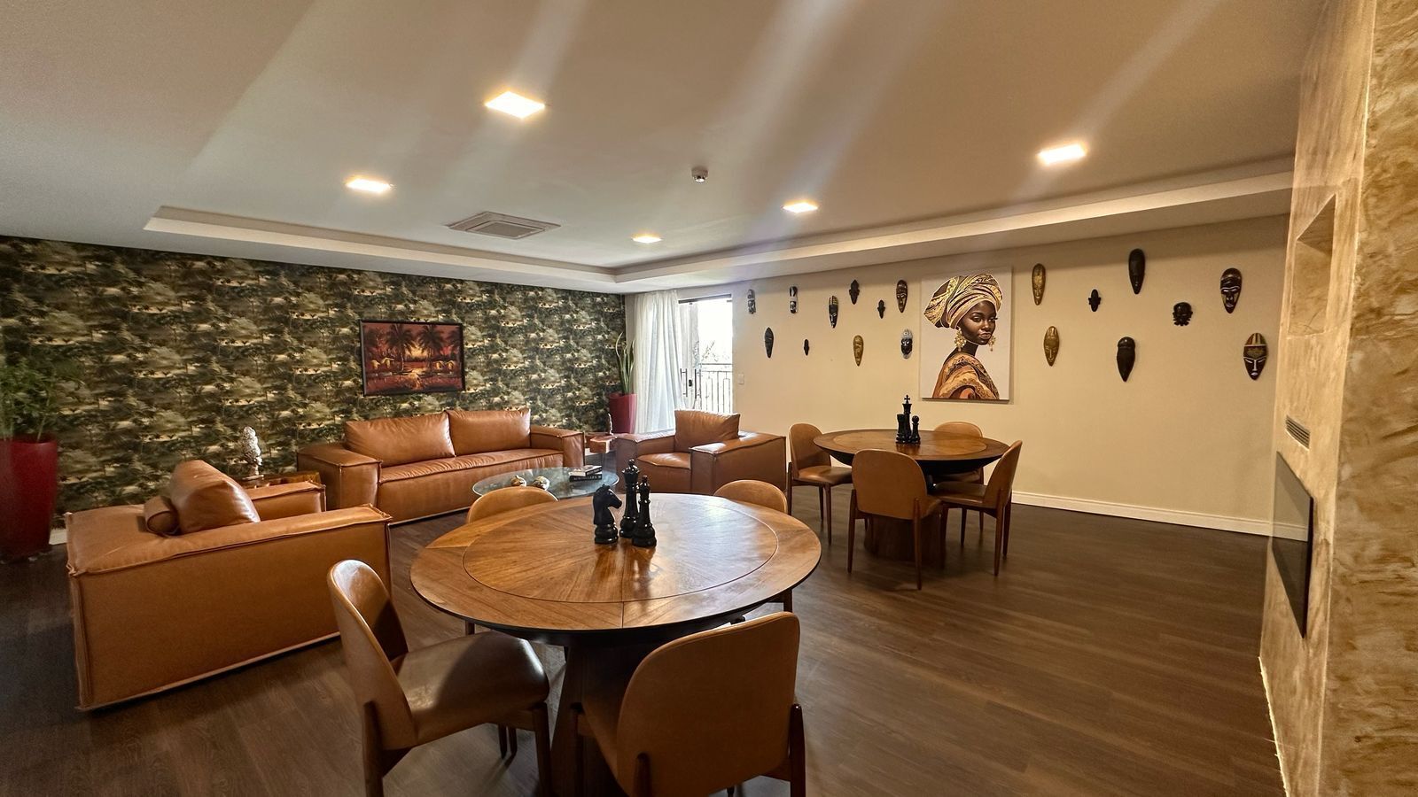 Ein modernes Wohnzimmer mit einem runden Holztisch, Ledersofas und einer Steinwand mit dekorativen Masken.