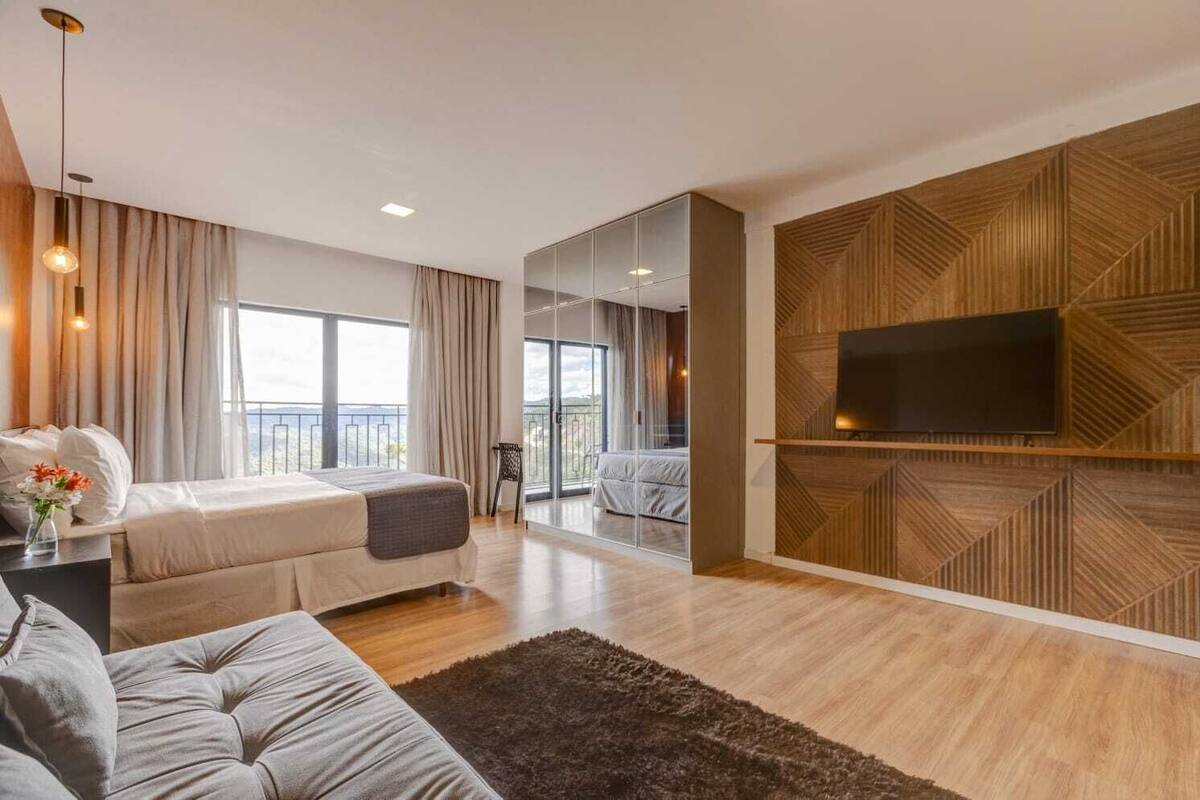 Ein modernes Hotelzimmer mit Bett, Sofa und Fernseher, der an einer Wand mit geometrischem Muster angebracht ist.