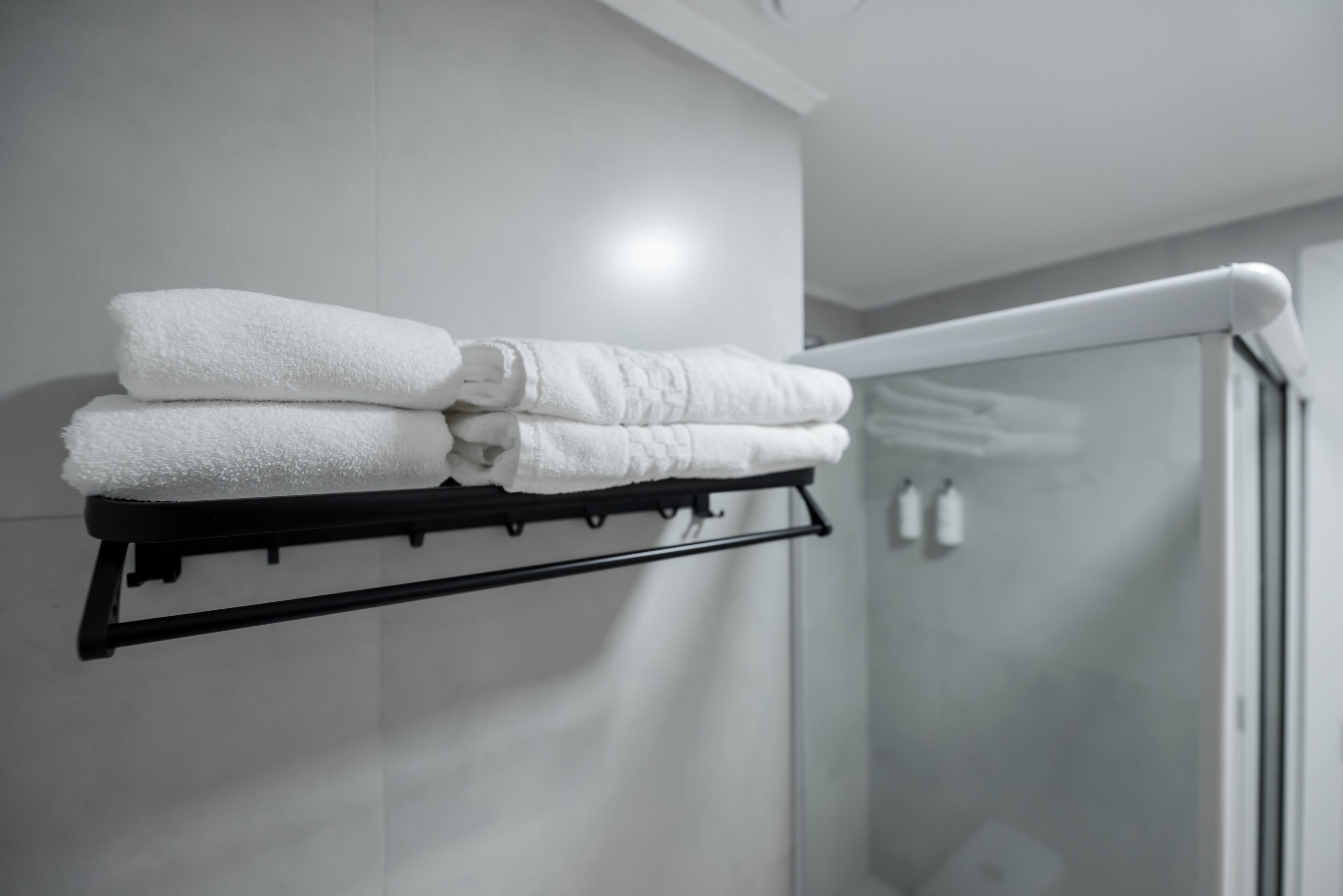 Une salle de bain avec une porte de douche en verre, un porte-serviettes avec des serviettes pliées et un mur blanc.