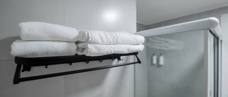 Une salle de bain avec une porte de douche en verre, un porte-serviettes avec des serviettes pliées et un mur blanc.