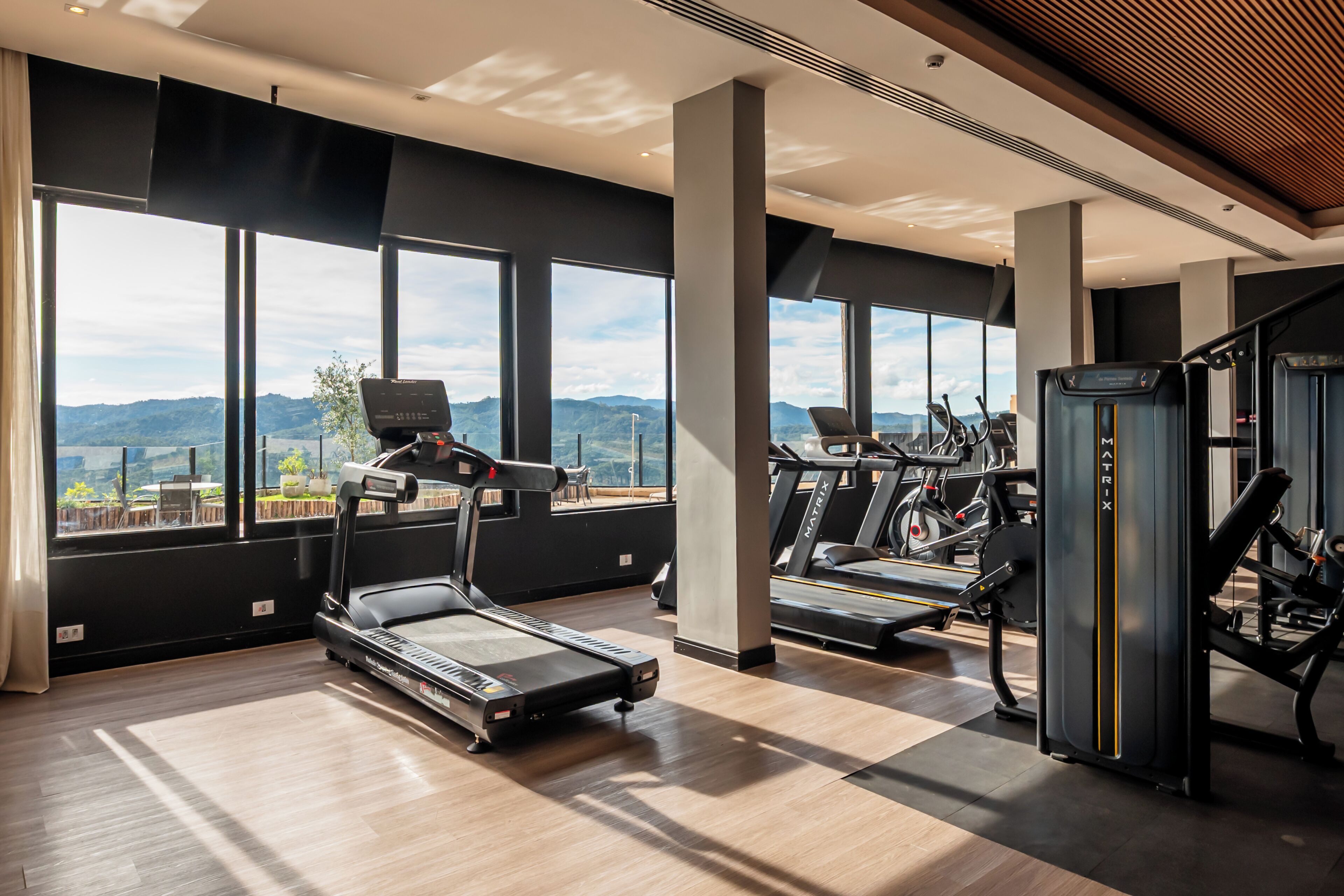 A gym with treadmills, a weight machine, and large windows offering a mountain view.
