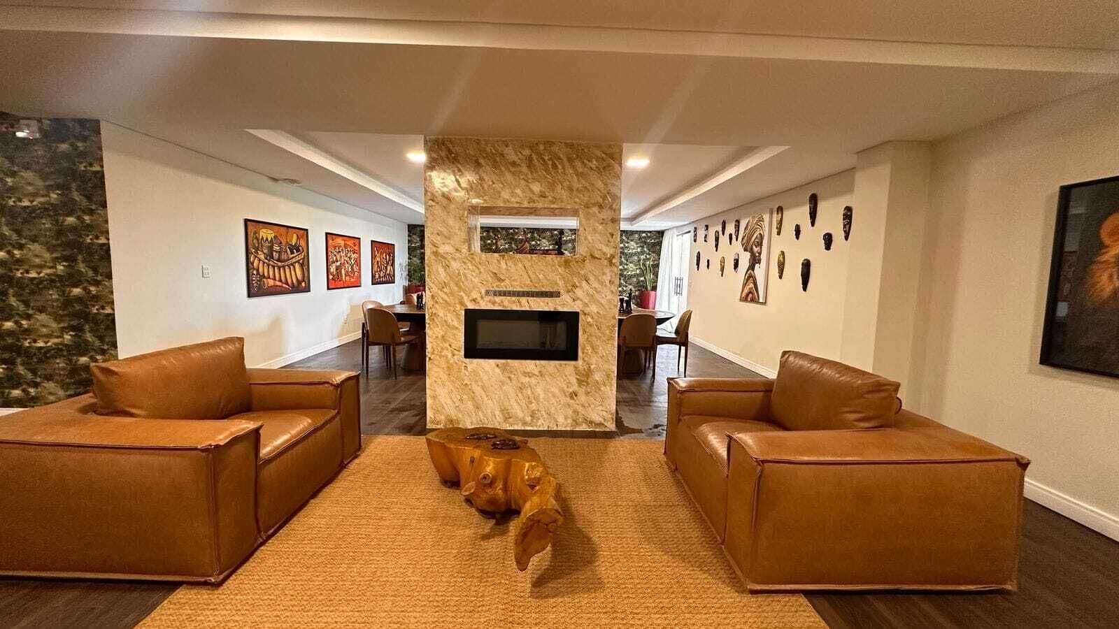A modern living room with two leather sofas, a central wooden coffee table, a fireplace, and artwork on the walls.