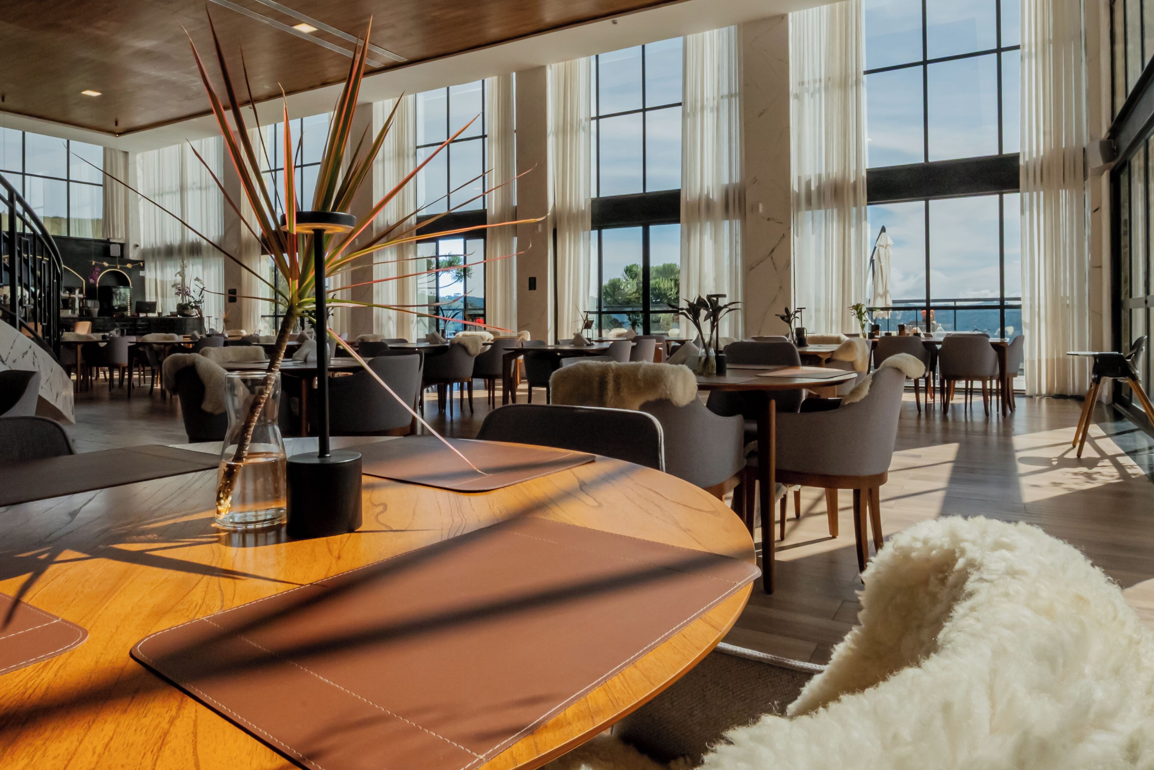 A spacious hotel lobby with large windows, a central round table, and multiple seating areas.