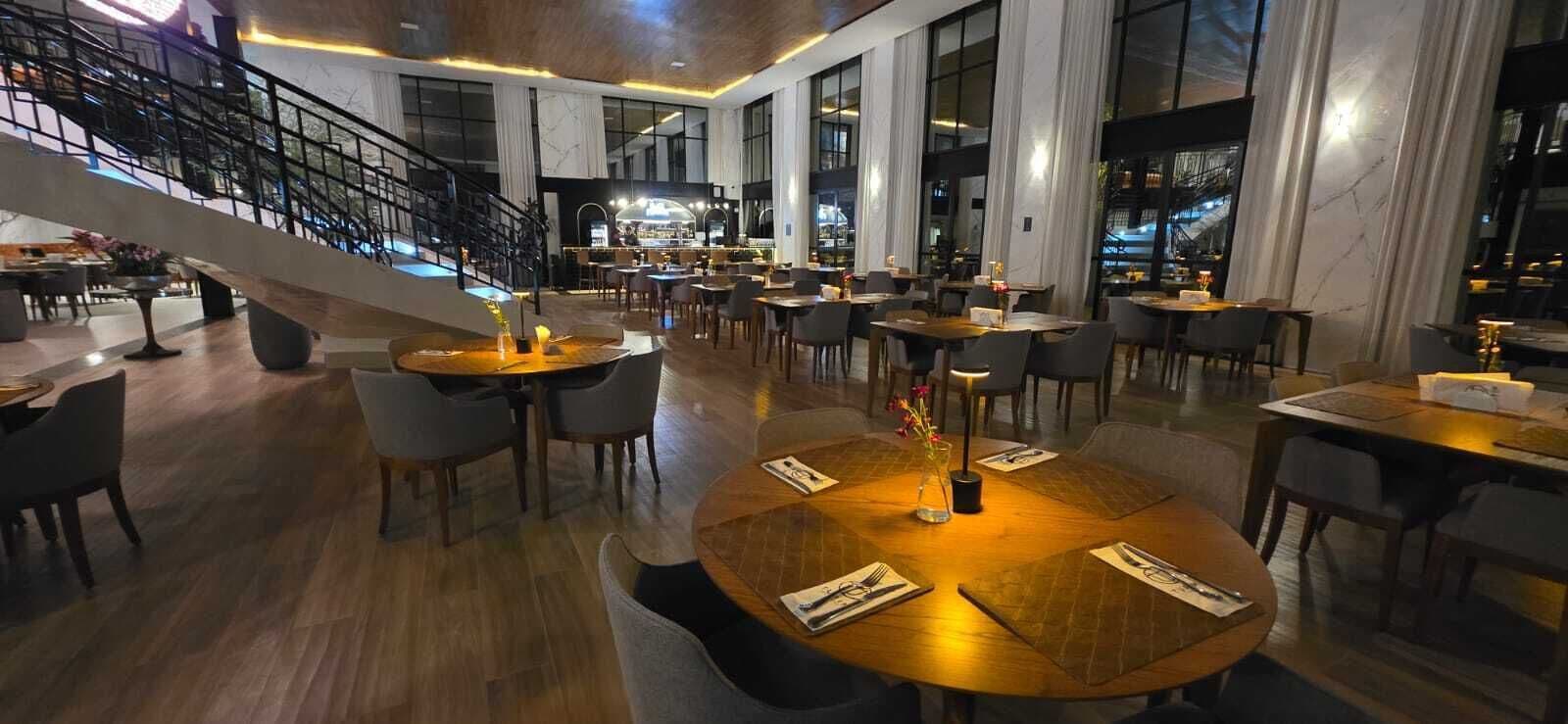 A spacious restaurant with multiple dining tables, a staircase, and large windows.
