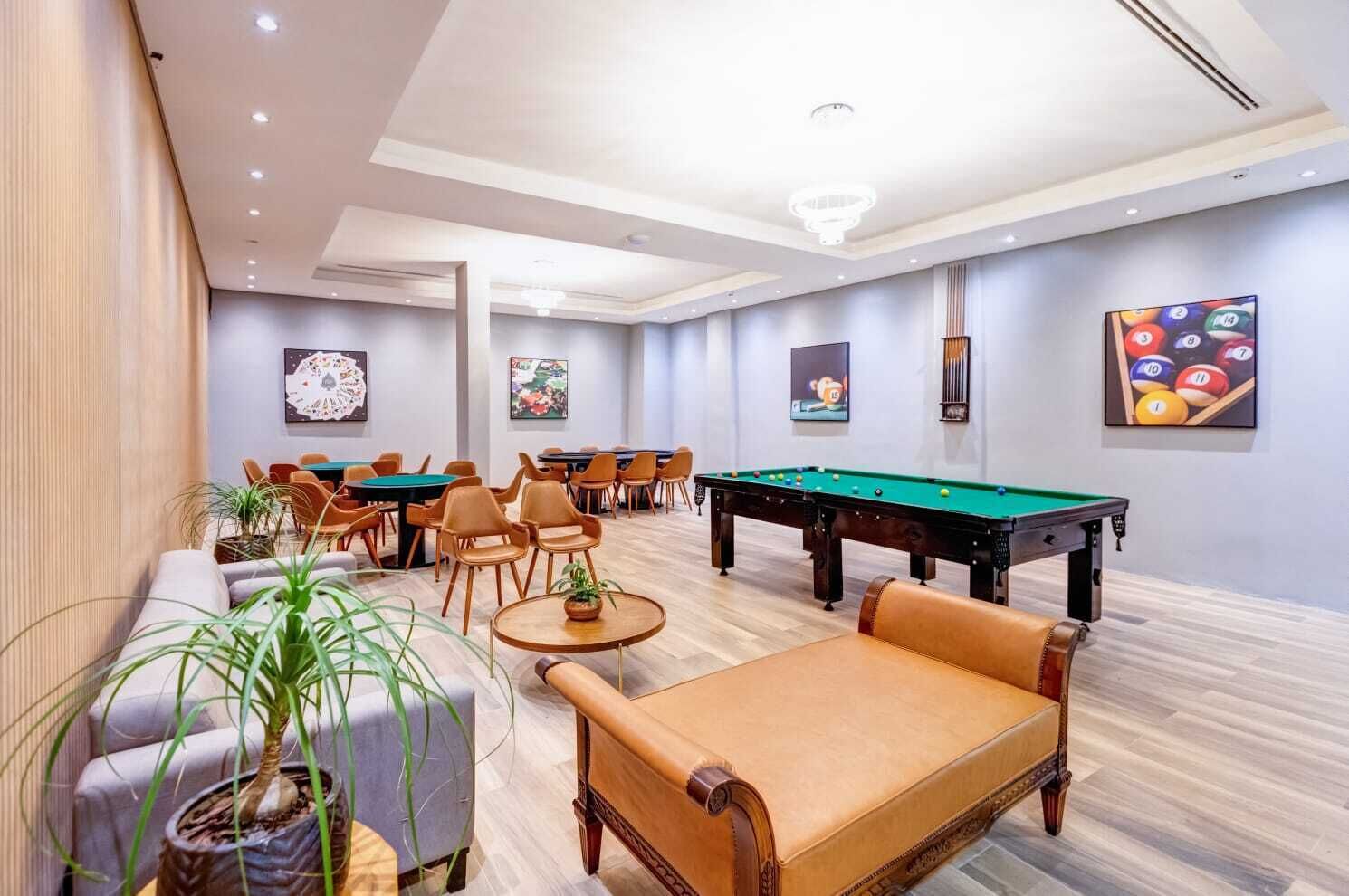 A room with a pool table, multiple chairs, a sofa, and potted plants.