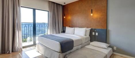 Habitación de hotel con una cama grande, una cama más pequeña, un balcón con cortinas y una lámpara moderna.
