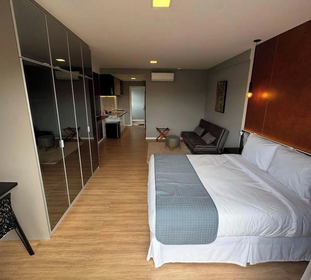 A hotel room with a large bed, a seating area with a sofa and armchairs, a small table, and a mirrored closet.