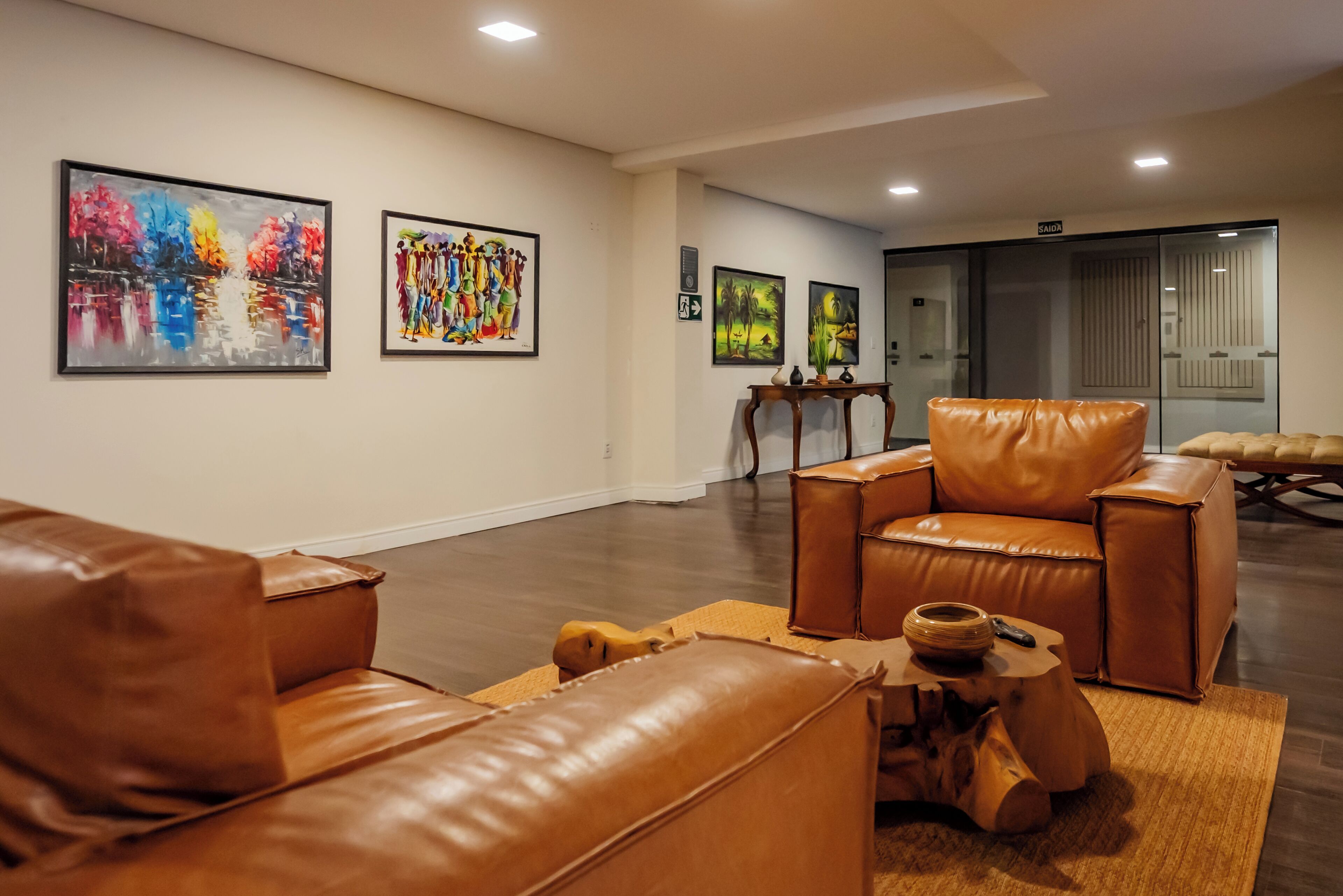 Uma área de estar moderna com sofás de couro, uma mesa de centro de madeira e obras de arte nas paredes.