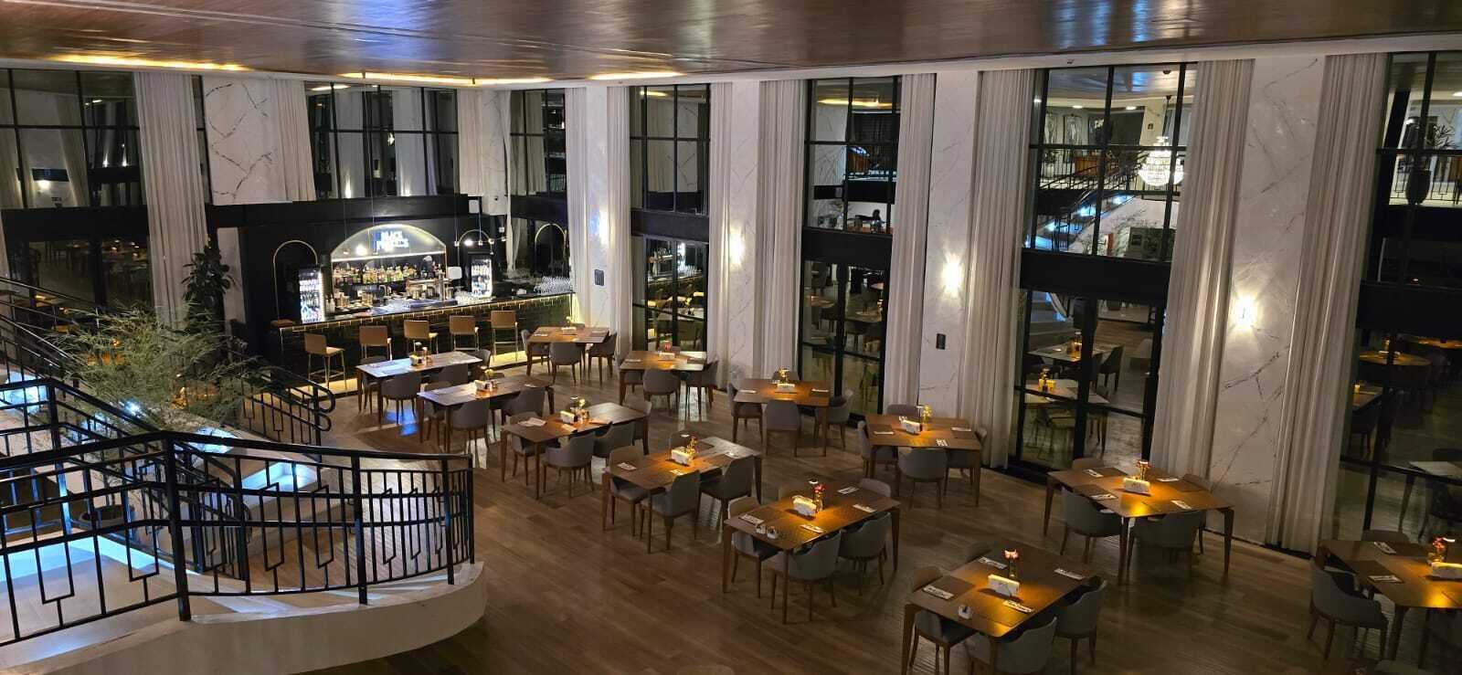 A hotel lobby with a bar area, multiple dining tables, and a staircase.