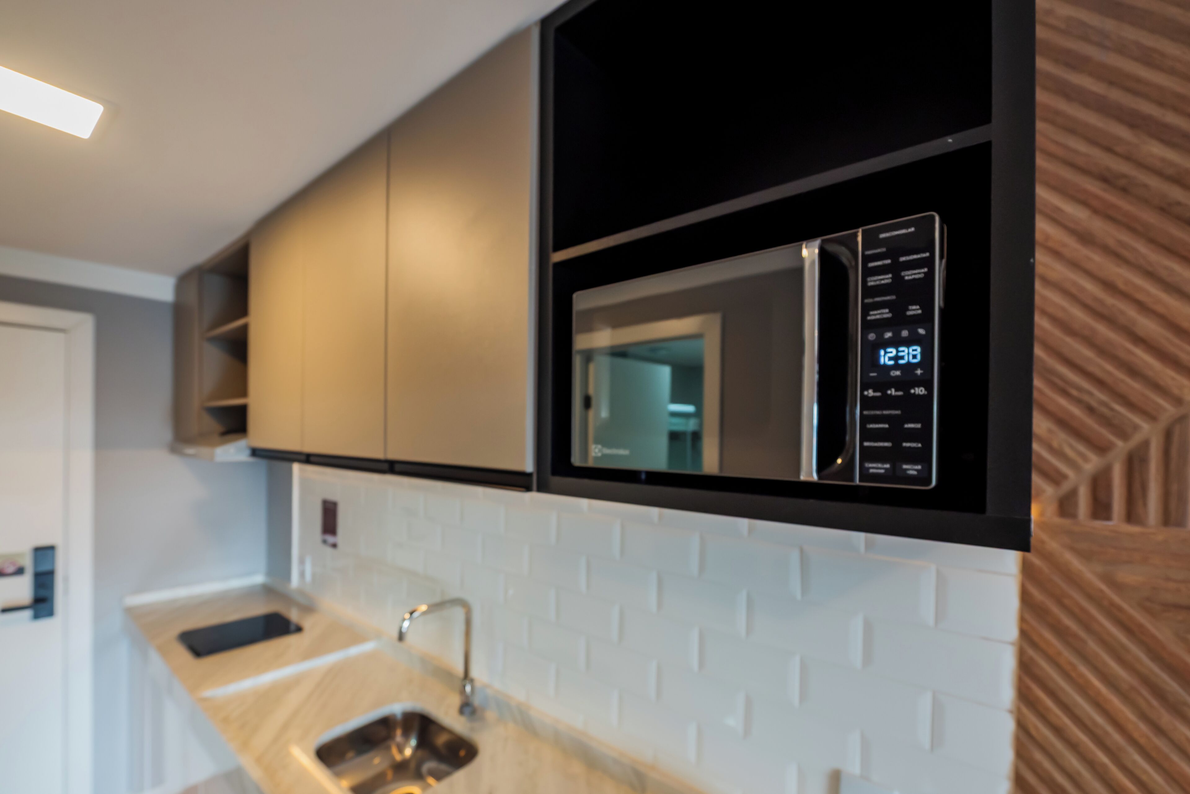 A modern kitchen with a built-in microwave, a stainless steel sink, and a white tiled backsplash.