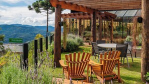 Une pergola en bois avec une table et des chaises, entourée d’une végétation luxuriante et offrant une vue sur les montagnes.