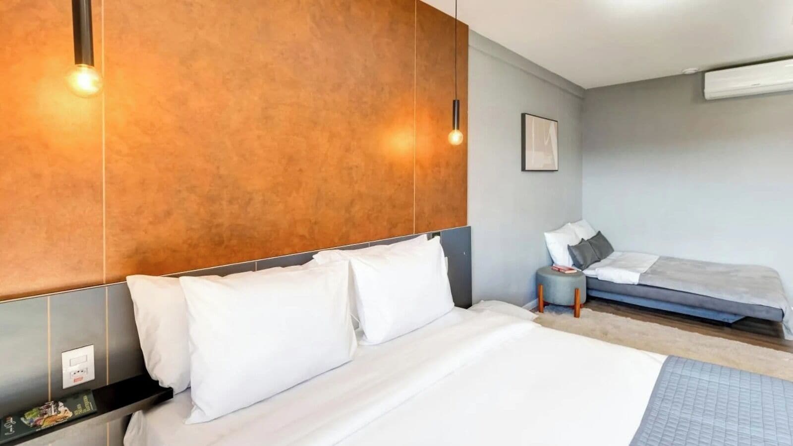 A hotel room with a large bed, a smaller bed, a nightstand, and a wall-mounted shelf.