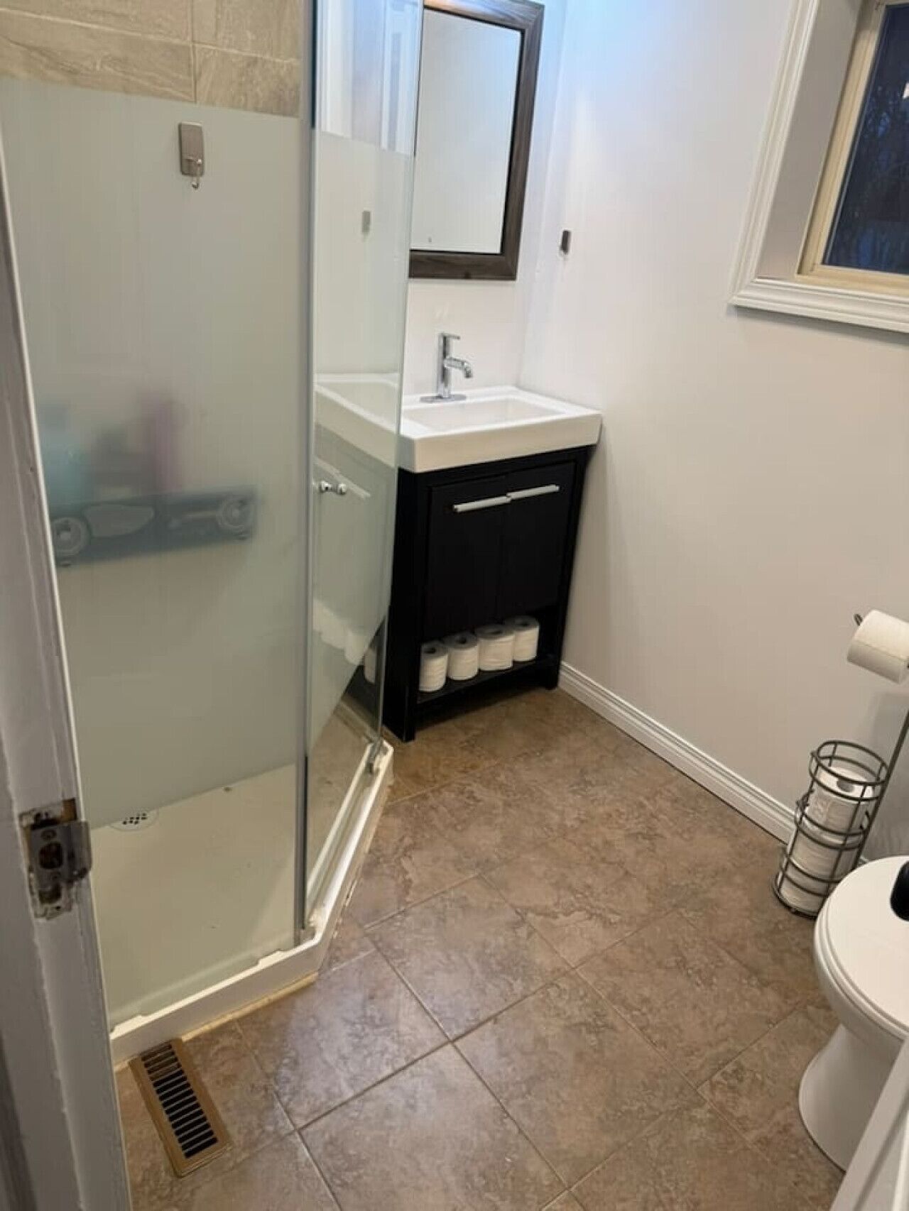 Une salle de bain avec une douche à parois de verre, un lavabo blanc avec un miroir au-dessus et des toilettes.