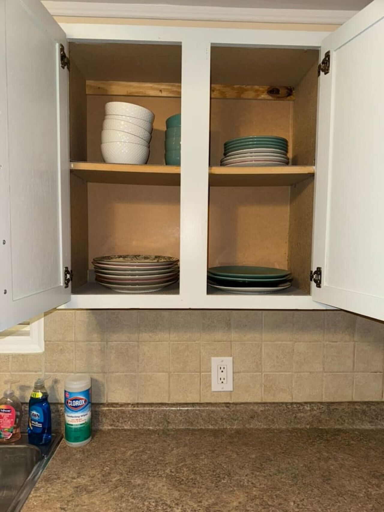 A kitchen with two open cabinets containing stacked plates and bowls.