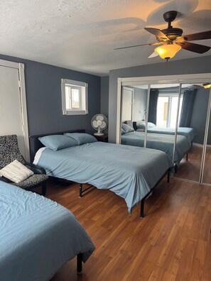 A bedroom with a bed, a chair, a ceiling fan, a window, and a mirror.