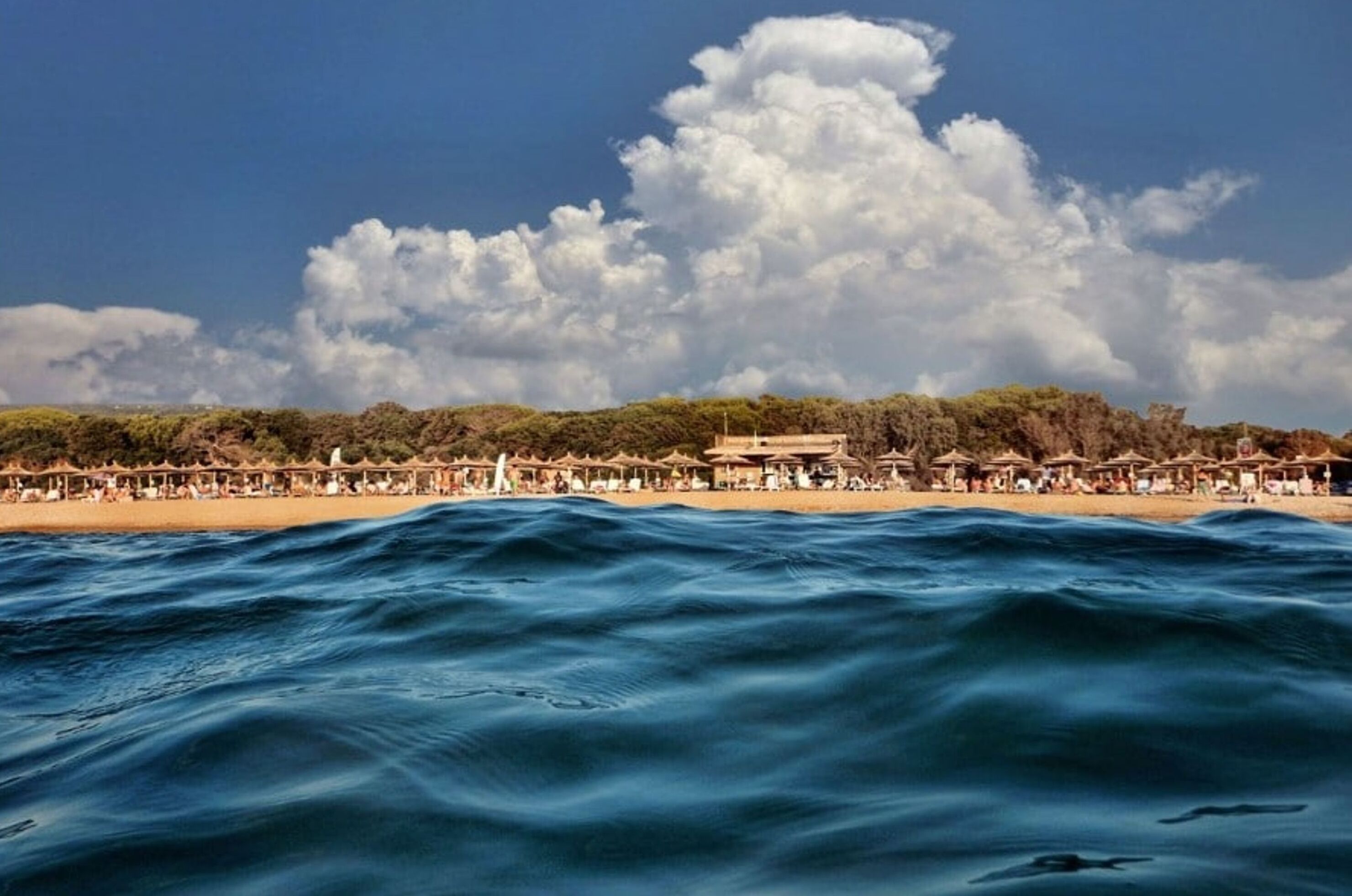 Una platja amb ombrelles i gent, un edifici al fons i un cel ennuvolat.