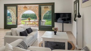 A living room with a white sofa, a coffee table, and a TV. There is a stone archway leading to an outdoor area with a table and chairs.