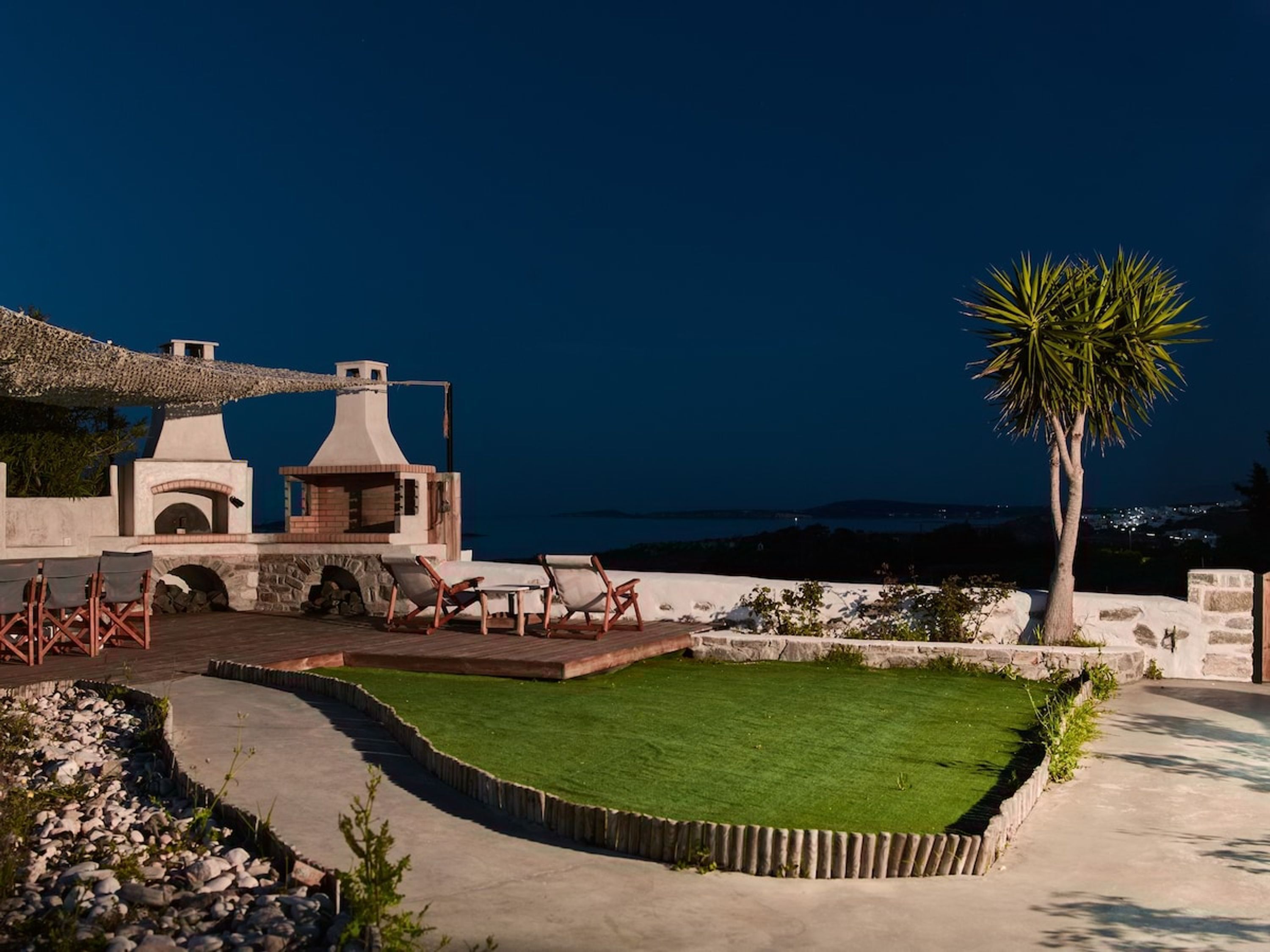 A rooftop terrace with outdoor seating, a small garden, and a view of the sea at dusk.