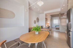 A modern kitchen with a central island, a dining area with a wooden table and chairs, and a living space with a sofa and a coffee table. - Michael Zeppos Studio 1, Naousa (Naousa)