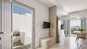 A modern kitchen with a built-in oven, a dining area with a table and chairs, and a large window offering a city view. - Michael Zeppos Studio 1, Naousa (Naousa)