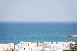 Une ville côtière aux bâtiments blancs, bordée d’une mer d’un bleu limpide, avec une montagne qui se profile à l’horizon.
