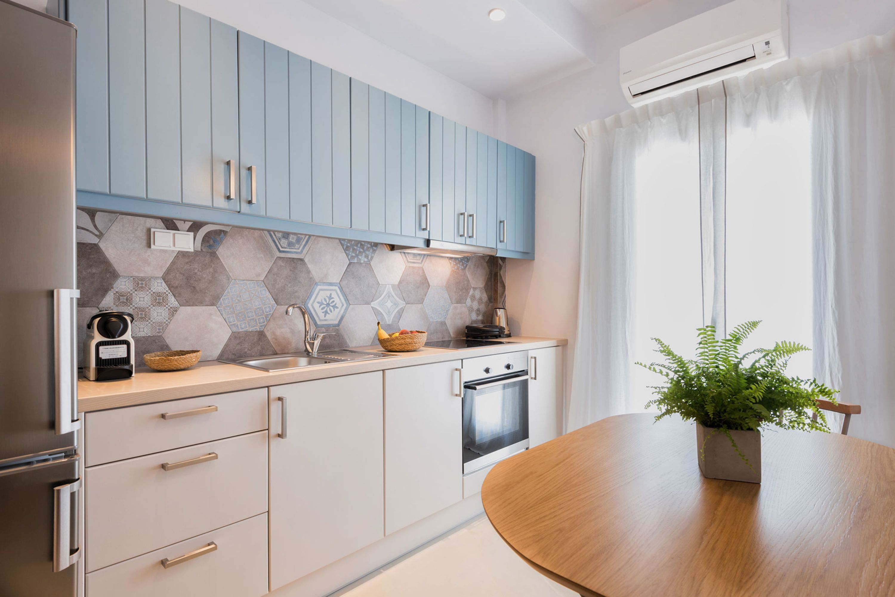 Una cocina moderna con armarios azul claro, salpicadero de azulejos hexagonales y una mesa de comedor de madera con una planta en maceta.