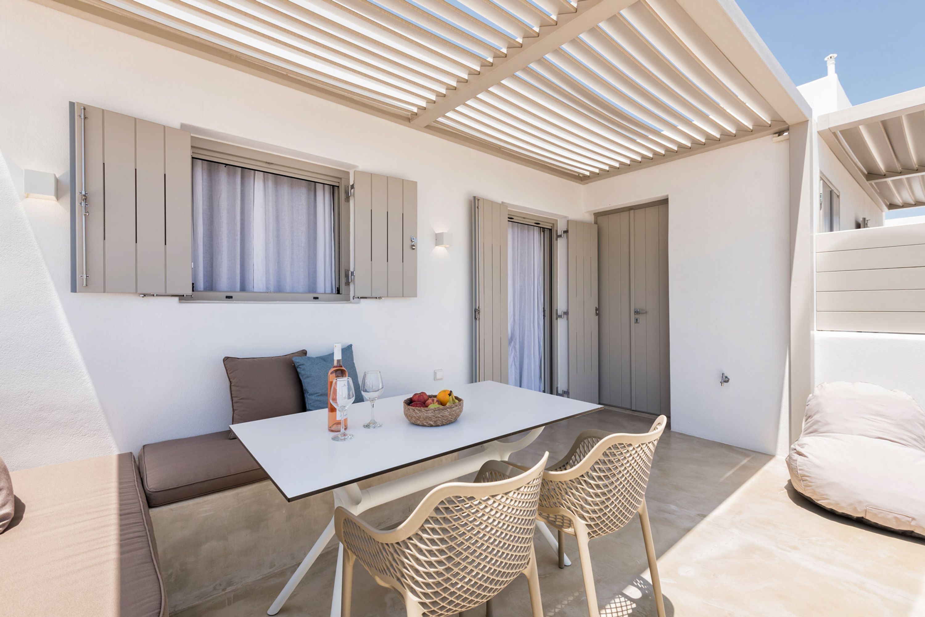 A modern outdoor dining area with a white table, wicker chairs, and a cushioned bench.