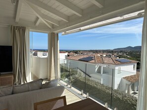 A balcony with a glass railing, a sofa, and a TV. - Sardinian villa with swimming pool, barbecue and sea view (Budoni)
