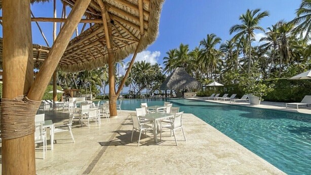 Un espace piscine doté de chaises longues, d’une structure à toit de chaume et de palmiers.