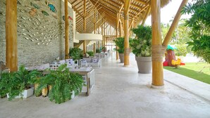 Un espace extérieur abrité, aménagé avec des tables et des chaises, des plantes en pot et un mur de pierre décoré de motifs de poissons.