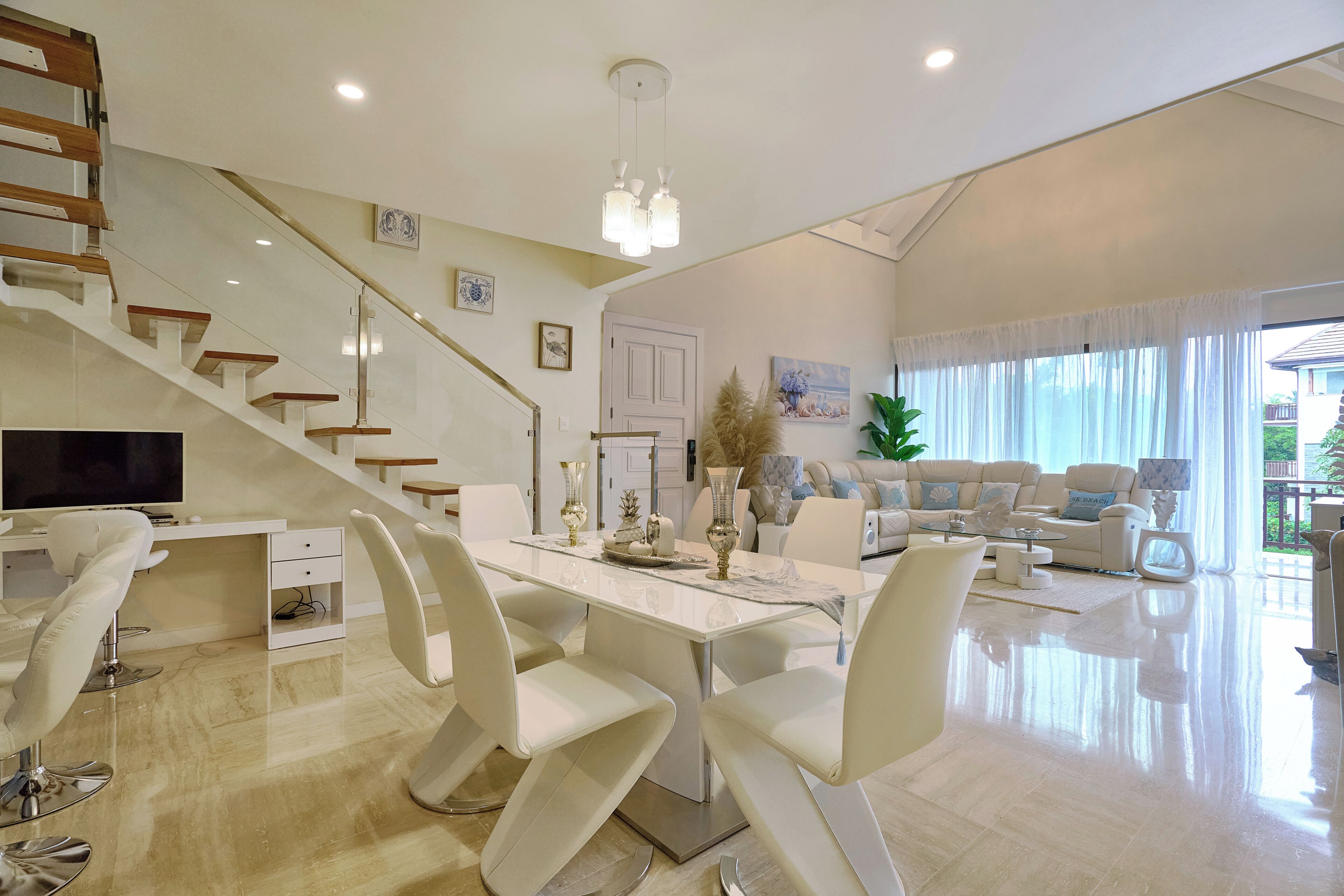 Un amplio espacio habitable con una mesa de comedor, sillas blancas, un sofá y una escalera.