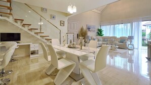 Un vaste espace de vie comprenant une table à manger, des chaises blanches, un canapé et un escalier.